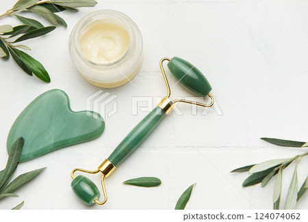 Gua sha stone, face roller and cream promoting skin care and relaxation 124074062