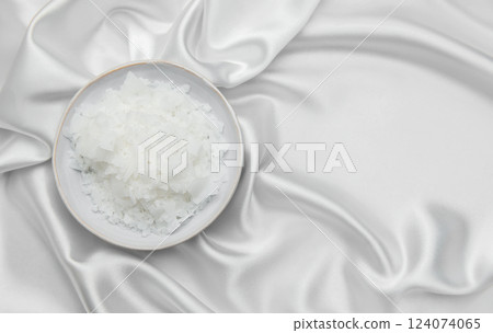 Magnesium flakes in a bowl resting on elegant white silk fabric 124074065