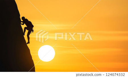 Climber ascends steep rock face at sunset against vibrant orange sky 124074332