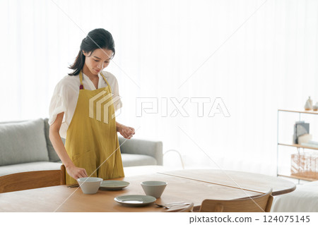 A woman in an apron putting dishes on the table 124075145