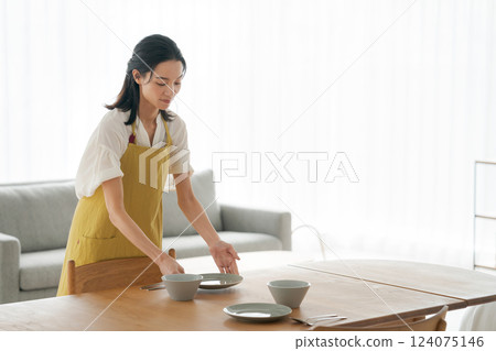 A woman in an apron putting dishes on the table A woman in an apron putting dishes on the table 124075146