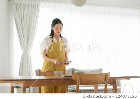 A woman in an apron putting dishes on the table 124075150