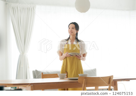 A woman in an apron putting dishes on the table 124075153