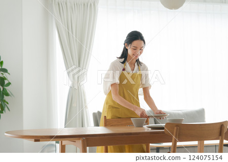 一位穿著圍裙的女人把盤子放到桌上 一位穿著圍裙的女人把盤子放到桌上 124075154