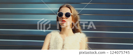Modern stylish young woman in white fur vest, glasses, fashionable girl posing on gray background Modern stylish young woman in white fur vest, glasses, fashionable girl posing on gray background 124075745