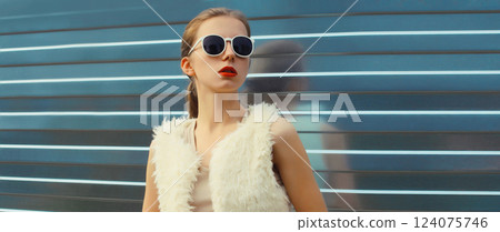 Modern stylish young woman in white fur vest, glasses, fashionable girl posing on gray background 124075746
