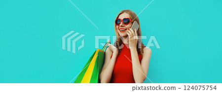 Beautiful happy young woman calling on smartphone with shopping bag looking away on blue background Beautiful happy young woman calling on smartphone with shopping bag looking away on blue background 124075754