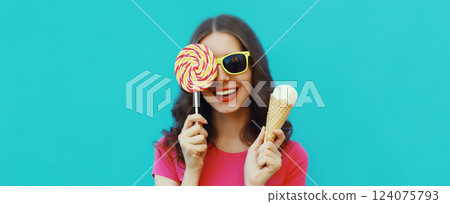 Summer portrait happy young woman holding ice cream cone, lollipop blowing kiss on blue background Summer portrait happy young woman holding ice cream cone, lollipop blowing kiss on blue background 124075793