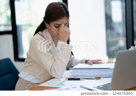 Stressed young businesswoman overwhelmed by paperwork with finance, market charts and documents in office 124075805