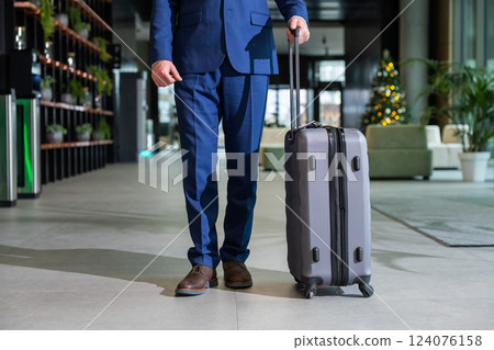 Man in blue suit standing with a big suitcase 124076158