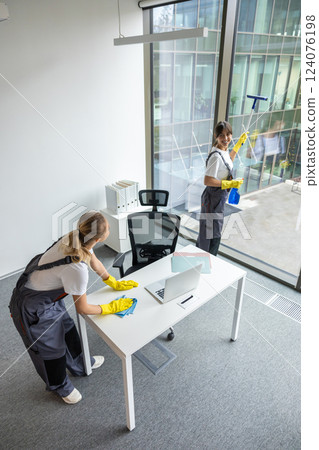 Blonde young woman in yellow gloves cleaning the table in the office Blonde young woman in yellow gloves cleaning the table in the office 124076198
