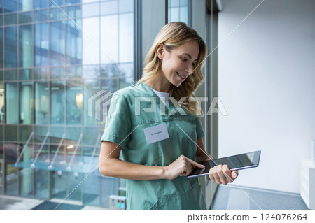 Female healthcare worker standing near window in hospital using modern technology Female healthcare worker standing near window in hospital using modern technology 124076264