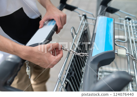 Unrecognizable man taking trolley at store unfastening cart Unrecognizable man taking trolley at store unfastening cart 124076440