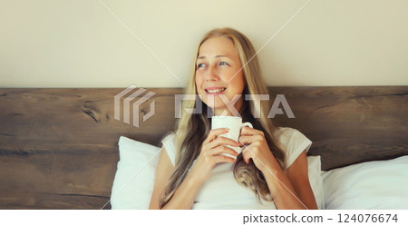 Happy smiling mature woman enjoying with cup of hot coffee lying on bed at home Happy smiling mature woman enjoying with cup of hot coffee lying on bed at home 124076674