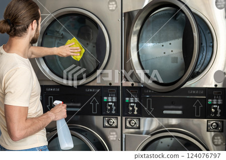 Male cleaning washing machine and dryer in laundromat Male cleaning washing machine and dryer in laundromat 124076797
