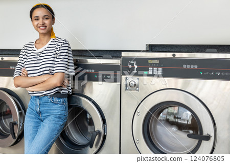 Woman in launderette using washing machine to clean her clothes 124076805