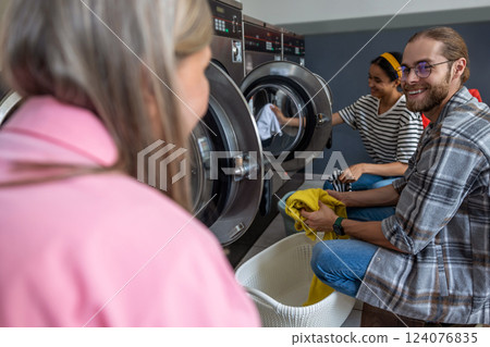 Women and man in modern laundromat washing garments and textiles 124076835