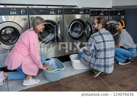 People in laundromat organizing fresh garments after completing housework chores People in laundromat organizing fresh garments after completing housework chores 124076836