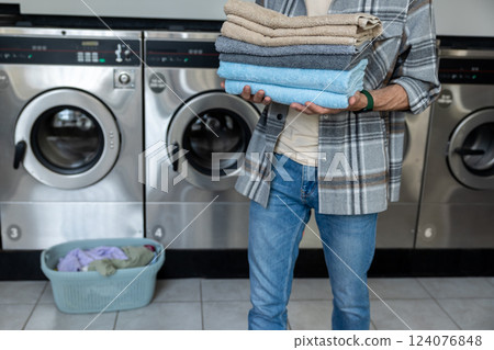 Anonymous male in self-service laundry using washing machine to clean her towels Anonymous male in self-service laundry using washing machine to clean her towels 124076848