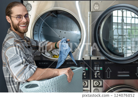 Man in public laundromat loading dirty clothes into washing machine 124076852