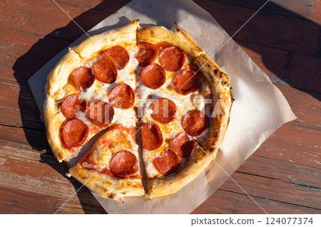 Delicious Pepperoni Pizza with Melted Cheese on a Wooden Surface, Perfectly Cut and Ready to Enjoy, Ideal for Sharing with Friends and Family, Classic Italian Favorite 124077374