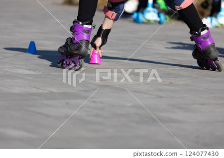 A Young Skater Perfecting Their Skills with Cones on a Clear, Bright Day in a City Park, Wearing Colorful Roller Skates and Practicing Balance and Coordination Skills. 124077430