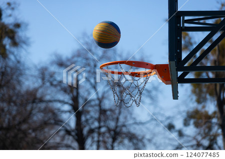 Dynamic Moment Captured: A Colorful Basketball Aiming for a Hoop Against a Clear Sky with Bare Trees in the Background 124077485