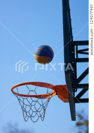 Dynamic Moment: A Colorful Basketball Aiming for the Hoop Against a Clear Blue Sky in an Outdoor Setting 124077497
