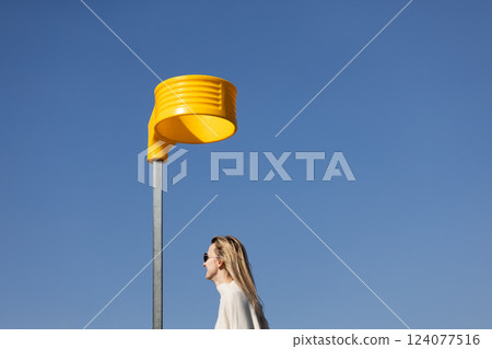 A Unique Perspective: A Stylish Woman Walking Beneath a Brightly Colored Yellow Structure Against a Clear Blue Sky A Unique Perspective: A Stylish Woman Walking Beneath a Brightly Colored Yellow Structure Against a Clear Blue Sky 124077516