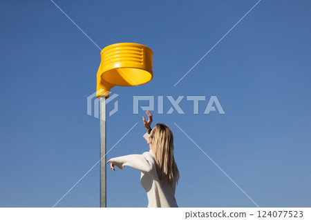 A Modern Artistic Encounter with an Eye-Catching Yellow Structure Against a Clear Blue Sky Featuring a Woman Engaging with the Unique Design A Modern Artistic Encounter with an Eye-Catching Yellow Structure Against a Clear Blue Sky Featuring a Woman Engaging with the Unique Design 124077523