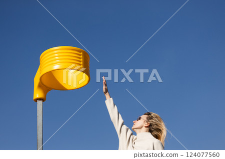 A Woman Reaching for a Unique Yellow Object Against a Bright Blue Sky in a Sunny Outdoor Setting, Embodying a Spirit of Playfulness and Curiosity to Inspire Creativity A Woman Reaching for a Unique Yellow Object Against a Bright Blue Sky in a Sunny Outdoor Setting, Embodying a Spirit of Playfulness and Curiosity to Inspire Creativity 124077560