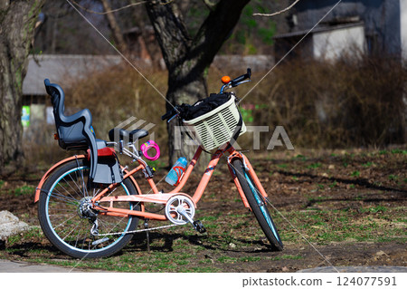 Charming Pink Bicycle with Child Seat and Basket Nestled Among Nature's Beauty on a Sunny Day in the Park Charming Pink Bicycle with Child Seat and Basket Nestled Among Nature's Beauty on a Sunny Day in the Park 124077591