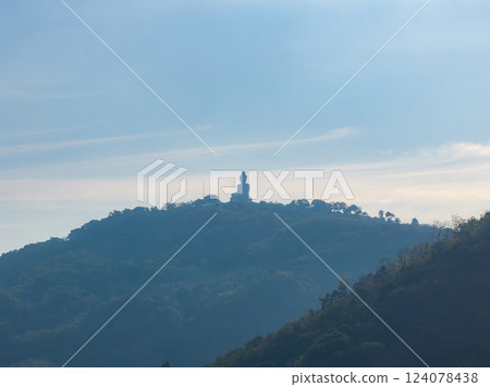 The Big Buddha statue stands atop a hill in Phuket, Thailand, surrounded by lush greenery and silhouetted against a soft, hazy sky. The Big Buddha statue stands atop a hill in Phuket, Thailand, surrounded by lush greenery and silhouetted against a soft, hazy sky. 124078438