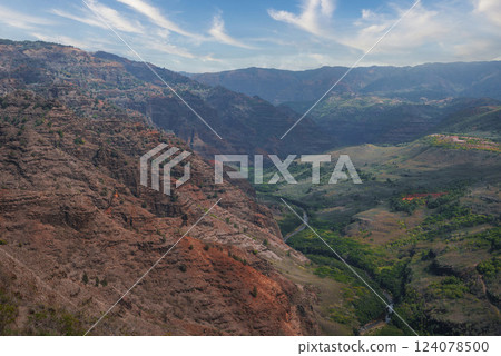 View of Waimea Canyon on Kauai, Hawaii, featuring red and brown canyon walls, a winding river, green vegetation, and a clear sky with wispy clouds. View of Waimea Canyon on Kauai, Hawaii, featuring red and brown canyon walls, a winding river, green vegetation, and a clear sky with wispy clouds. 124078500