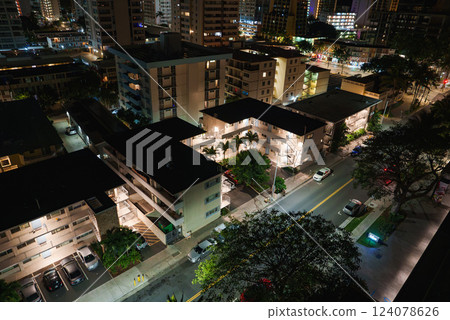 Urban scene at night with mid rise apartments, illuminated windows, parked cars, tropical greenery, and well lit streets in Honolulu, Hawaii. 124078626