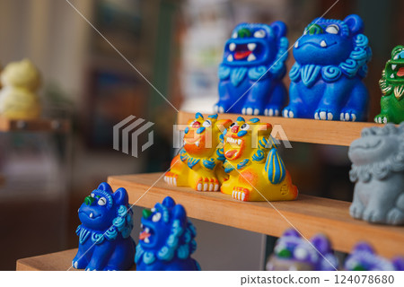 Vibrant blue and yellow ceramic lion figurines with intricate details displayed on wooden shelves in an indoor setting, likely a shop or market in Thailand. 124078680