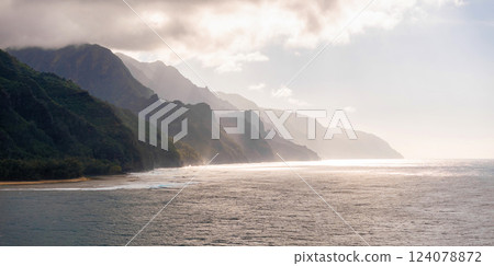 The Napali Coast on Kauai Island features rugged cliffs, lush greenery, a secluded beach, and misty mountain ridges meeting the Pacific Ocean. 124078872