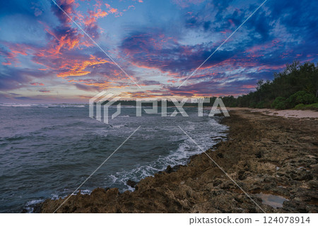 A coastal scene at sunset with rocky shoreline, sandy beach, lush greenery, and vibrant pink, purple, and orange hues in the sky. A coastal scene at sunset with rocky shoreline, sandy beach, lush greenery, and vibrant pink, purple, and orange hues in the sky. 124078914