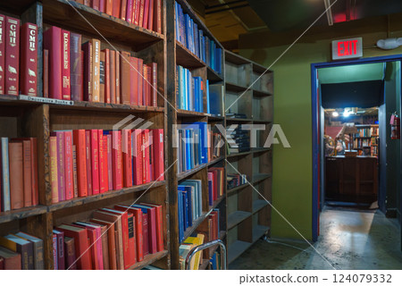Wooden bookshelves filled with red and blue books create a striking contrast. An exit sign above a doorway leads to more books, enhancing the labyrinthine feel. 124079332