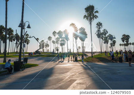 Venice Beach in Los Angeles at sunset features iconic palm trees casting long shadows. People walk, bike, and enjoy the skate park and grassy areas. Venice Beach in Los Angeles at sunset features iconic palm trees casting long shadows. People walk, bike, and enjoy the skate park and grassy areas. 124079503