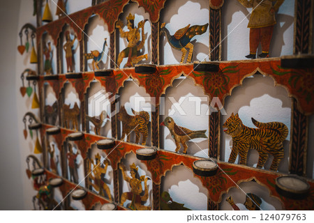 The image features a wall display with arched niches, each holding hand painted figures of animals and humans, adorned with floral patterns in vibrant colors. 124079763