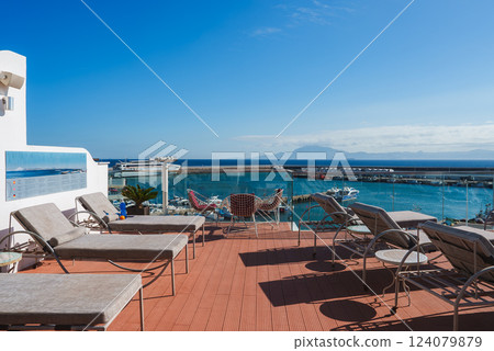 A rooftop terrace features sun loungers and modern chairs, offering views of a marina with boats. Glass railings provide an unobstructed view of the water. A rooftop terrace features sun loungers and modern chairs, offering views of a marina with boats. Glass railings provide an unobstructed view of the water. 124079879