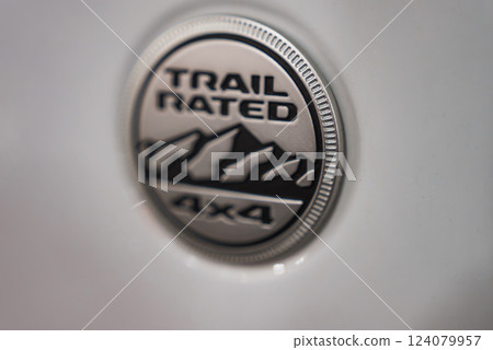 Circular metallic badge with Trail Rated text, mountain design, and 4x4 marking on a white vehicle body, emphasizing off road capability. Circular metallic badge with Trail Rated text, mountain design, and 4x4 marking on a white vehicle body, emphasizing off road capability. 124079957