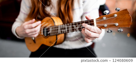 Female adult playing acoustic ukulele indoors Female adult playing acoustic ukulele indoors 124080609