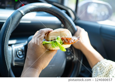 Asian woman driver hold and eat hamburger in car, dangerous and risk an accident. Asian woman driver hold and eat hamburger in car, dangerous and risk an accident. 124080657