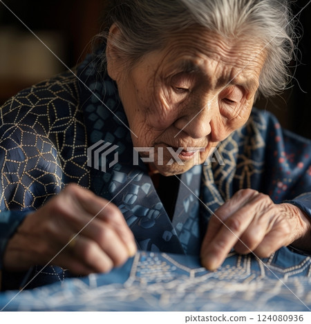 Elderly Japanese woman meticulously working on traditional Sashiko embroidery with precise, intricate stitches. 124080936