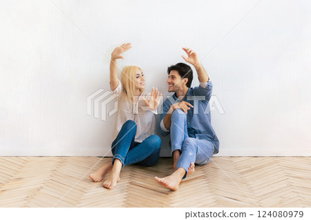 A young couple sits on the floor of a new home, framing the space with their hands. They are both smiling and looking at each other. A young couple sits on the floor of a new home, framing the space with their hands. They are both smiling and looking at each other. 124080979