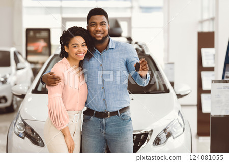 Joyful Black Couple Holding New Car Key Smiling At Camera Posing Standing Near Luxury Auto In Dealership Store 124081055