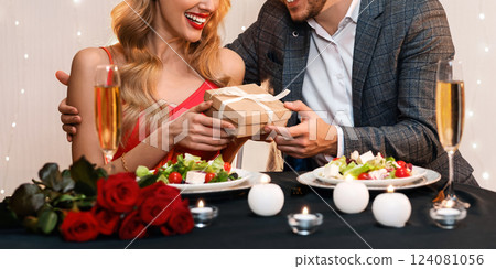 Valentine's Day Celebration. Loving man surprising his girlfriend with romantic gift at dinner in restaurant, free space Valentine's Day Celebration. Loving man surprising his girlfriend with romantic gift at dinner in restaurant, free space 124081056