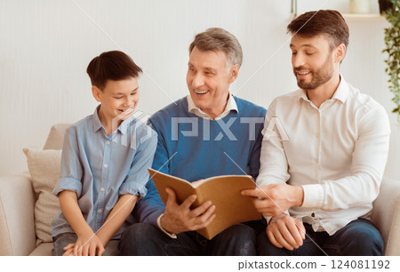 Little Boy, His Dad And Grandpa Reading Book Sitting On Sofa At Home. Weekend With Father And Grandfather. Selective Focus Little Boy, His Dad And Grandpa Reading Book Sitting On Sofa At Home. Weekend With Father And Grandfather. Selective Focus 124081192